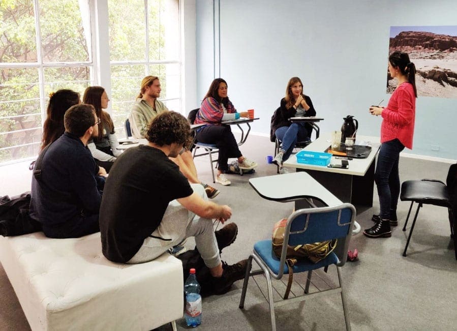 Varios alumnos recibiendo clase presencial impartida por una profesora.
